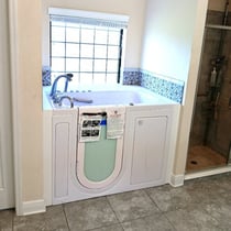 Newly installed white Ella walk-in tub with swing-open door beside a glass shower stall in a tiled bathroom