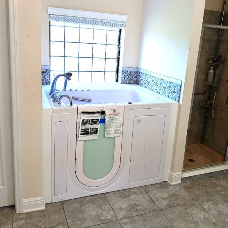 Newly installed white Ella walk-in tub with swing-open door beside a glass shower stall in a tiled bathroom