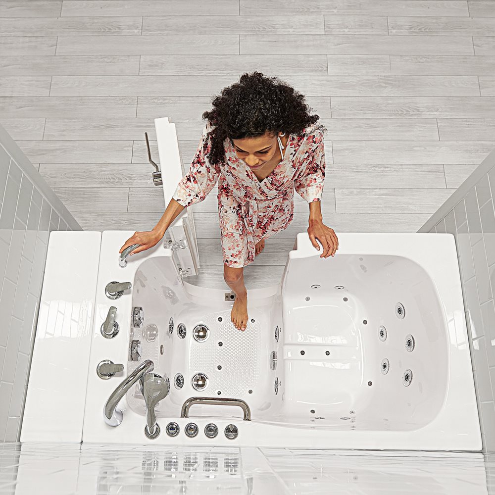 Aerial view of a woman stepping into an Ella Capri walk-in tub with its 3-latch outward swing door open