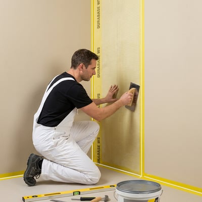 Instalador arrodillado aplicando membrana impermeabilizante en una esquina de pared de ducha con el sistema de impermeabilización Durabase WS.