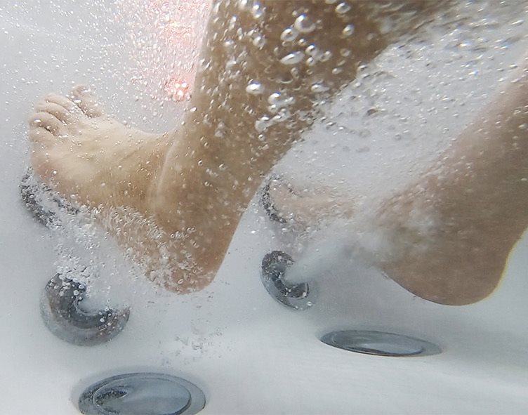 Vue sous-marine des pieds au-dessus des buses des jets d'air et des jets de balnéothérapie dans le bac à pieds d'une baignoire à porte Ella Elite
