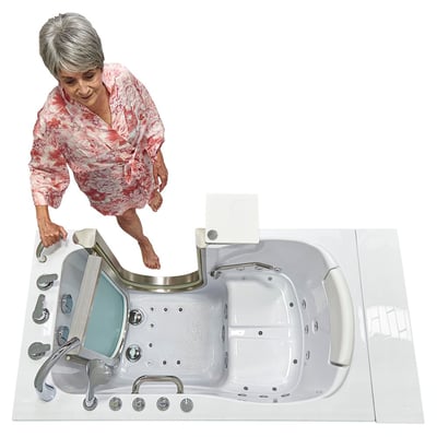 Senior woman in a floral robe stepping barefoot into an Ella Elite walk-in tub with open door, anti-slip floor, and swivel tray
