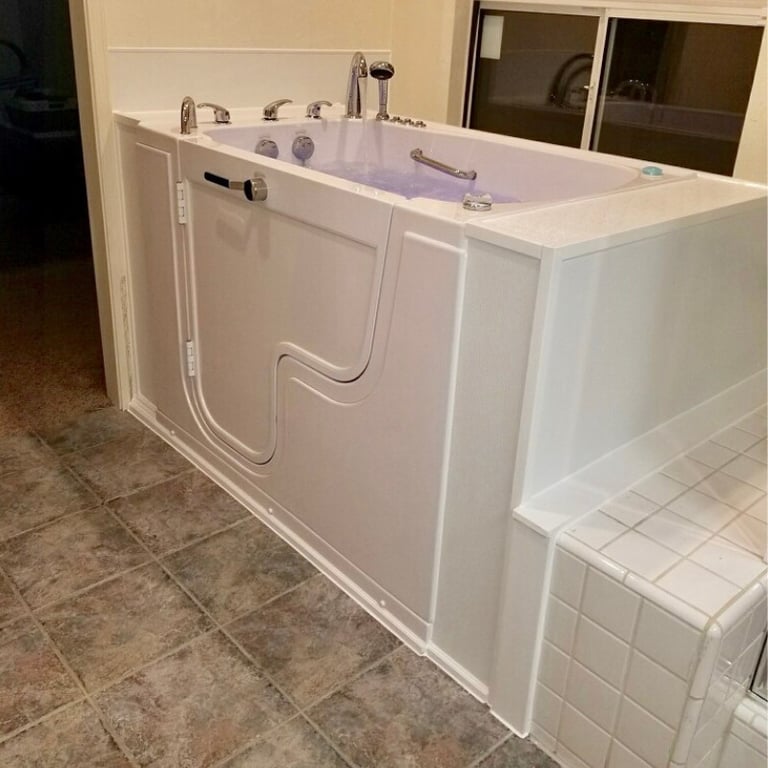 White Ella walk-in tub with inward swing door, chrome faucets, and hydro jets installed next to tiled step in a home bathroom