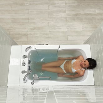 Mujer joven relajándose con los ojos cerrados en la bañera de acceso Ella Capri con chorros de hidroterapia y puerta de apertura hacia afuera.