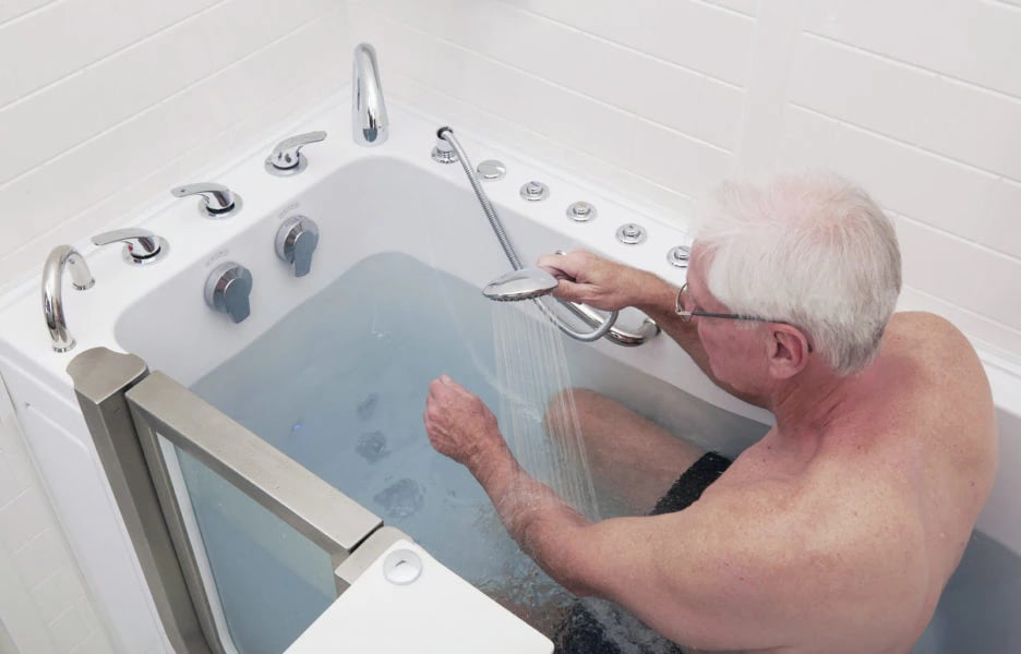 Senior man using a handheld showerhead while soaking in an Ella walk-in tub with hydrotherapy jets and chrome faucets