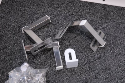 Ella walk-in tub extension panel kit hardware including stainless steel brackets, hinges, and mounting hardware laid out on dark surface