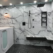 Luxury walk-in bathtub installation with marble walls, rain shower, built-in bench seat, and matte black fixtures
