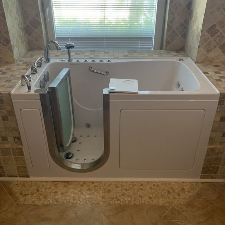 White Ella walk-in tub with open door showing air jets, grab bar, swivel tray, and chrome faucet installed in tiled bathroom