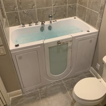 Ella walk-in tub filled with water and active jets installed in a tiled bathroom with chrome faucet fixtures