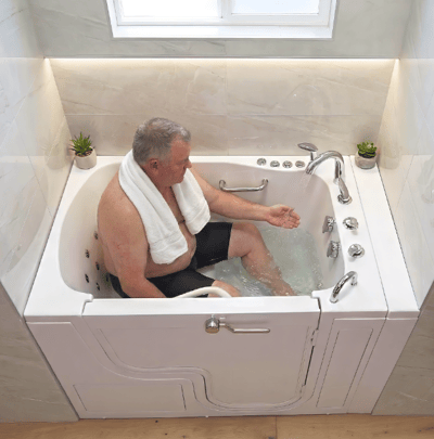 Middle-aged man with towel around neck testing warm water in an Ella walk-in tub with hydrotherapy jets and grab bars