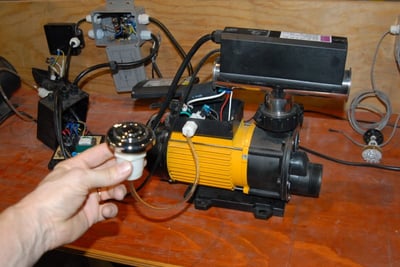 Technicien tenant une commande à bouton-poussoir connectée à un moteur de pompe à jet de baignoire à porte jaune sur un établi