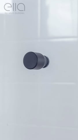 Gros plan d’un bouton de porte cylindrique noir mat sur le panneau de porte de douche coulissante encadrée Ella Duo