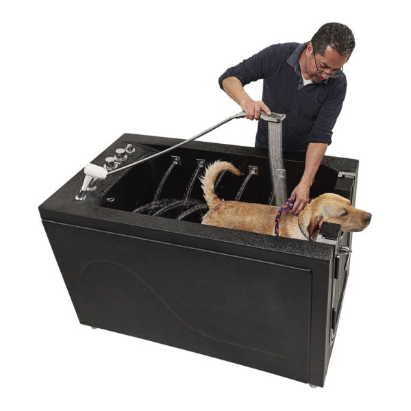 Man rinsing a golden retriever with a handheld sprayer inside the Ella therapeutic microbubble dog washing grooming station with side jets
