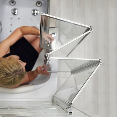 Woman reclining in a walk-in tub next to an open 4-fold tempered glass shower screen with chrome scissor-hinge frame