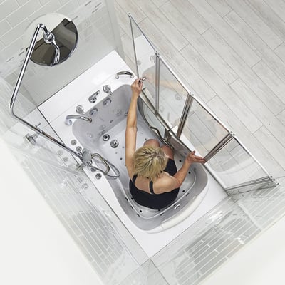 10″ Kit de tête de douche et colonne de douche pour robinets de baignoire encastrés dans le sol - Vue de dessus d’une femme assise dans une baignoire à porte Ella fermant la porte de douche pliante en verre avec kit de colonne de douche chromée