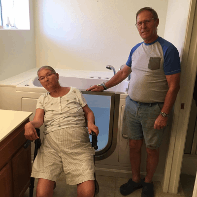 Senior woman in wheelchair and her husband posing beside their newly installed Ella walk-in tub with open door