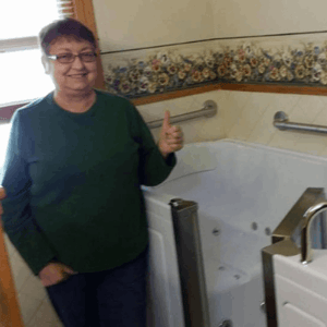 Walk In Tub Reviews Testimonials Feedback 30 Satisfied senior woman giving a thumbs up next to her newly installed walk-in tub with grab bars and jets