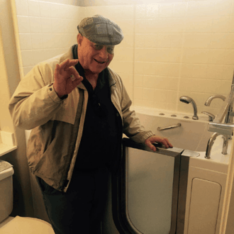 Walk In Tub Reviews Testimonials Feedback 4 Senior man smiling and giving an OK gesture while standing next to his installed Ella walk-in tub door