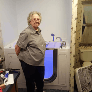 Walk In Tub Reviews Testimonials Feedback 42 Elderly woman standing proudly beside her newly installed walk-in tub with blue LED lighting in her home bathroom