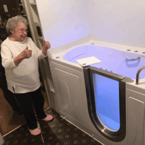 Walk In Tub Reviews Testimonials Feedback 48 Senior woman giving two thumbs up next to her new Ella walk-in tub with blue chromotherapy lighting and open door