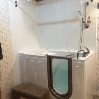 Walk In Tub Reviews Testimonials Feedback 6 White Ella walk-in tub with open door, grab bar, handheld shower, and white wall surround in a home bathroom
