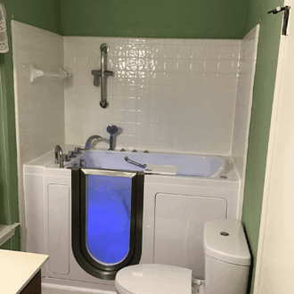 Walk In Tub Reviews Testimonials Feedback 9 Ella walk-in tub with blue chromotherapy lighting installed in a green and white tiled bathroom beside a toilet