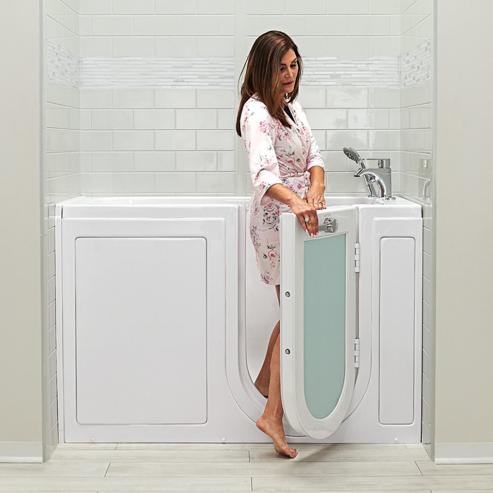 Woman in floral robe stepping into an Ella walk-in tub with outward swing door featuring a 3-latch seal system