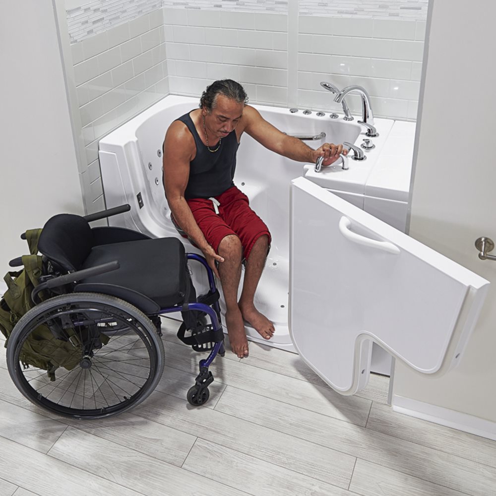 Wheelchair user transferring into an Ella walk-in tub through the wide outward-swing door with grab bar support
