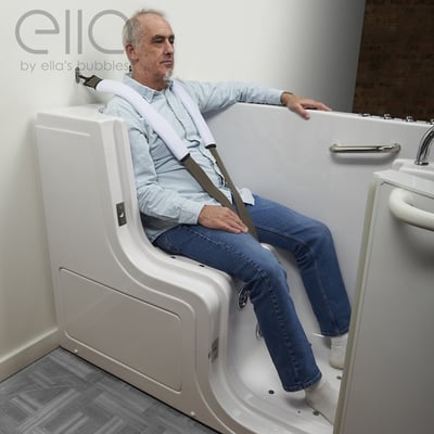 Senior man seated in an Ella walk-in tub demonstrating a safety seat belt harness strap for secure bathing support