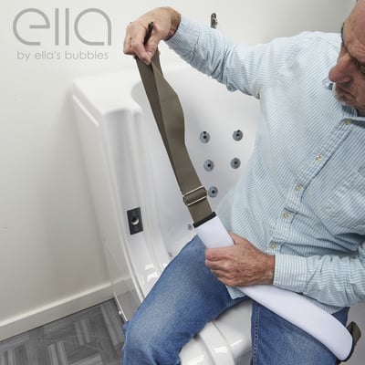 Senior man seated beside an Ella walk-in tub using a padded safety seat belt strap for added bathing stability