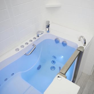 Vista aérea de una bañera de acceso directo Ella llena de agua con iluminación de cromoterapia azul, jets de hidroterapia y grifería cromada