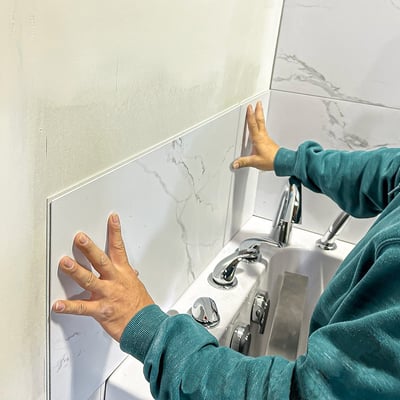 Installer pressing white marble-look Carrara wall panels into place around a walk-in tub surround during grout-free quick assembly installation