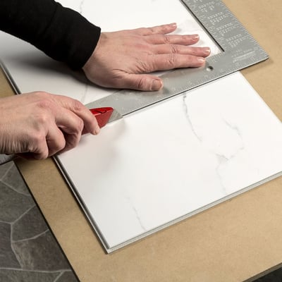Baldosa machihembrada de PVC Carrara de 25"x15" - Instalador marcando un panel de pared de ducha sin lechada con aspecto de mármol blanco Carrara con un cúter y una regla de acero