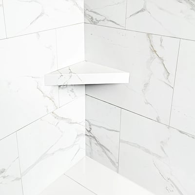 Baldosa machihembrada de PVC Carrara de 25"x15" - Primer plano de un estante de esquina blanco montado en paneles de pared de ducha con patrón de mármol de Carrara sin lechada en una cabina de ducha accesible