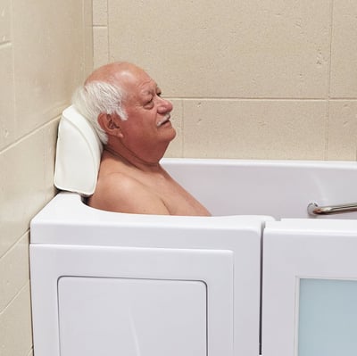 Hombre mayor sonriendo y relajándose apoyado en una almohada blanca para la cabeza con ventosas dentro de una bañera Ella