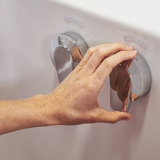 Mano de una persona mayor girando los pomos cromados de doble control de agua en la pared de una bañera de acceso Ella con indicadores de encendido y apagado.