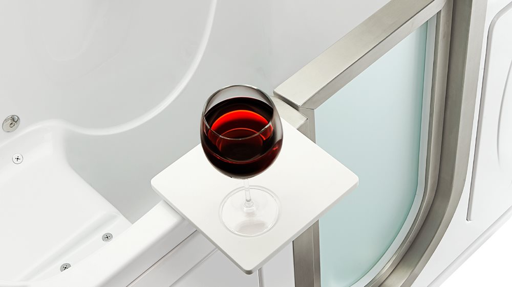 Red wine glass resting on the Ella walk-in tub swivel tray beside the stainless steel door frame