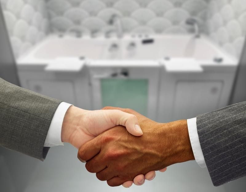 Two business professionals shaking hands in front of an Ella walk-in tub, representing a dealer partnership agreement