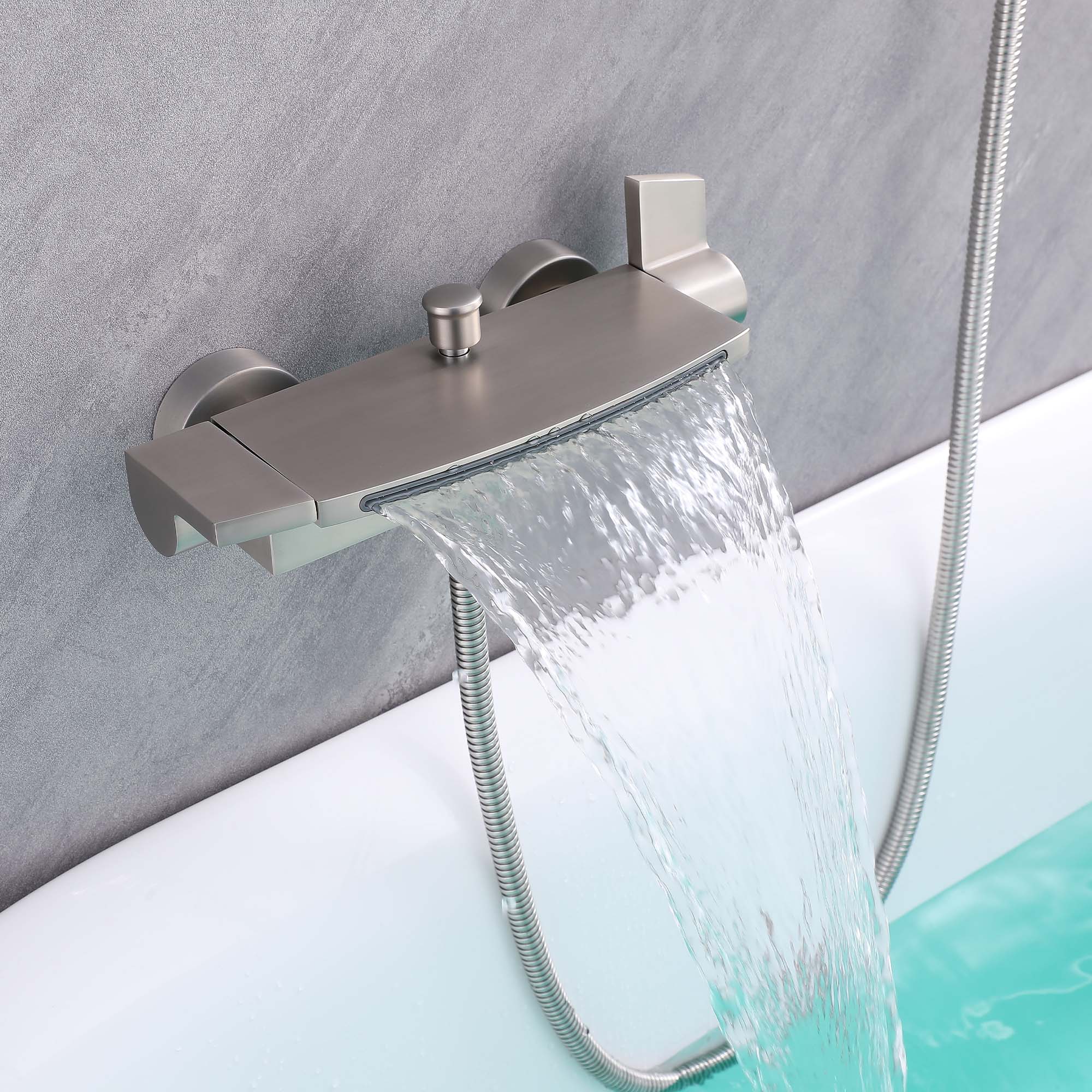 Brushed nickel thermostatic waterfall faucet flowing water into a walk-in tub with handheld shower hose mounted on gray wall