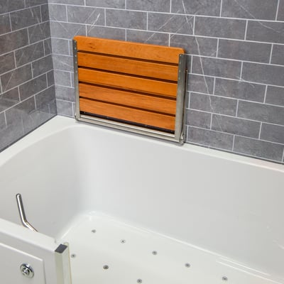 Teak wood folding shower seat mounted on gray tile wall above an Ella walk-in tub with air jet floor jets