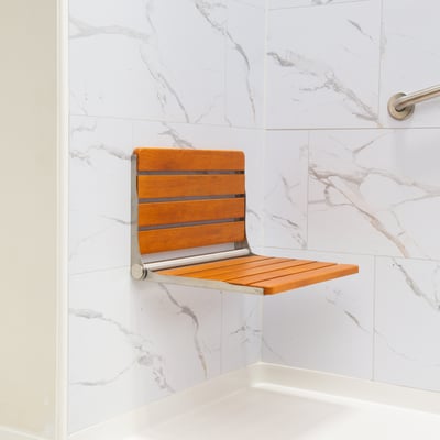Teak wood folding shower seat with stainless steel frame mounted on marble wall panel inside an accessible shower stall