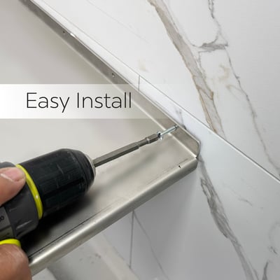Installer using a power drill to secure a stainless steel corner shower seat to marble wall panels