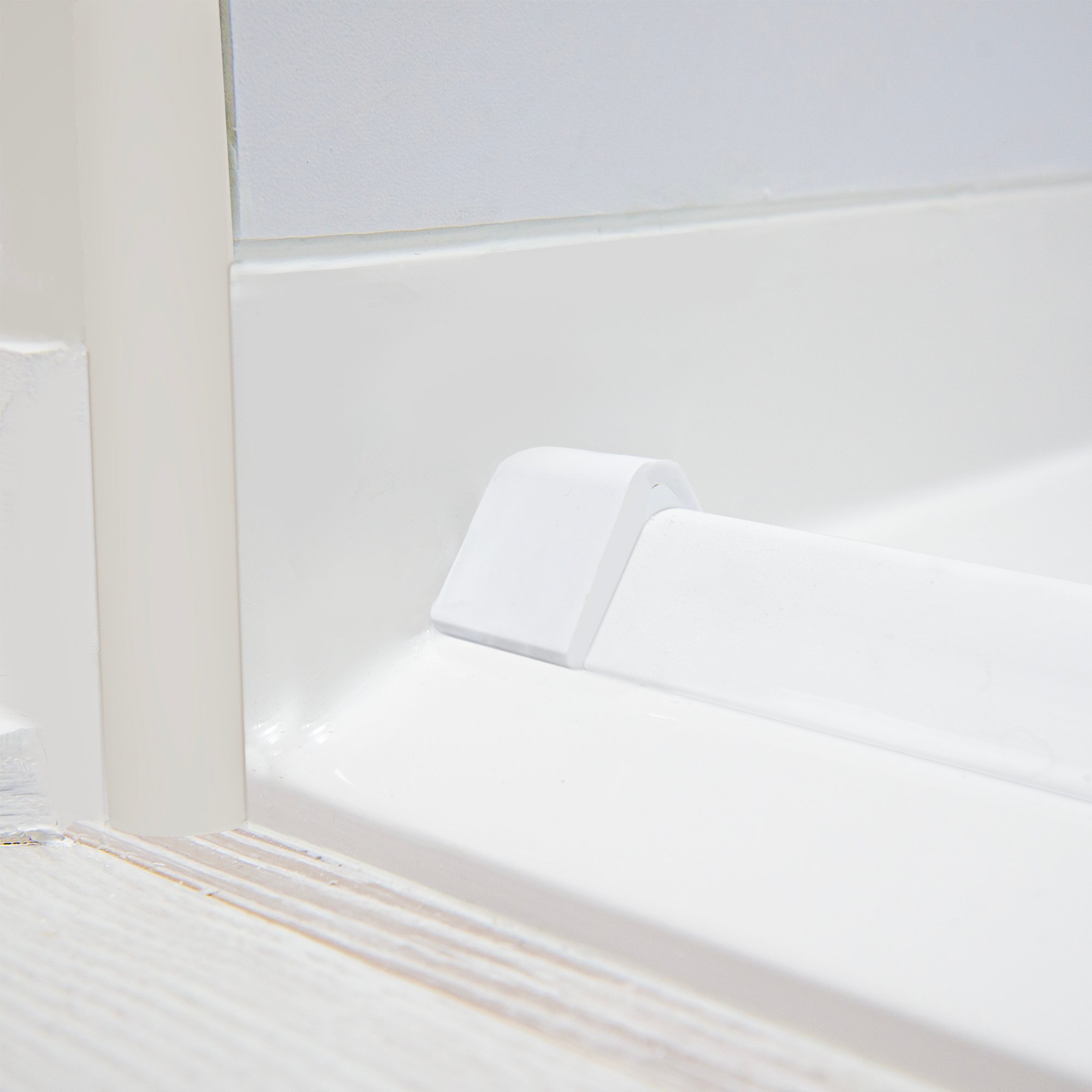 Close-up of a white collapsible rubber dam threshold installed at the entry of an Ella roll-in shower base