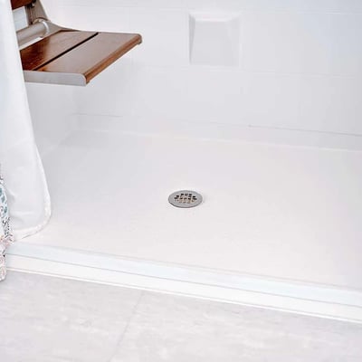 Primer plano de base de ducha accesible con desagüe central, presa de umbral plegable y asiento de ducha de teca plegable