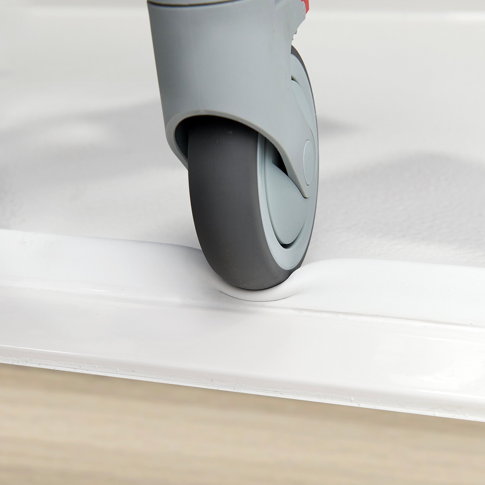 Shower chair wheel rolling over the collapsible rubber dam on an Ella barrier-free shower base