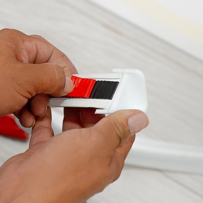 Manos despegando el respaldo adhesivo rojo de una presa de goma blanca para la instalación de acceso sin umbral en duchas a ras de suelo
