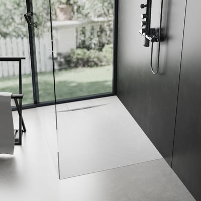 Modern walk-in shower stall with white low-profile shower pan, glass panel, and chrome fixtures overlooking a garden