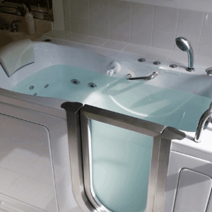 walk-in-tub-commentaires-temoignages-commentaires White Ella walk-in tub filled with water showing open stainless steel door, hydro jets, and handheld showerhead in tiled bathroom