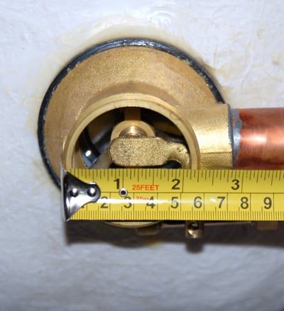 Close-up of a brass drain elbow fitting on a walk-in tub measured with a tape measure showing approximately 3 inches wide
