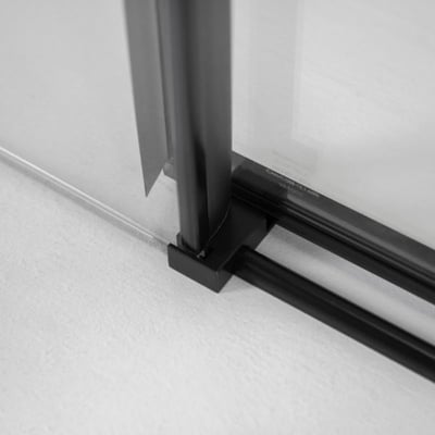 Primer plano del carril de la puerta de ducha corredera de vidrio templado con marco en negro mate y detalle de la esquina del riel de base